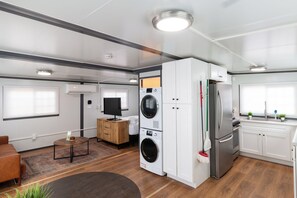 A modern RV interior with a kitchen, a washing machine, a refrigerator, and a flat-screen TV. - BoxHouse Executive Queen Suite (Monahans)
