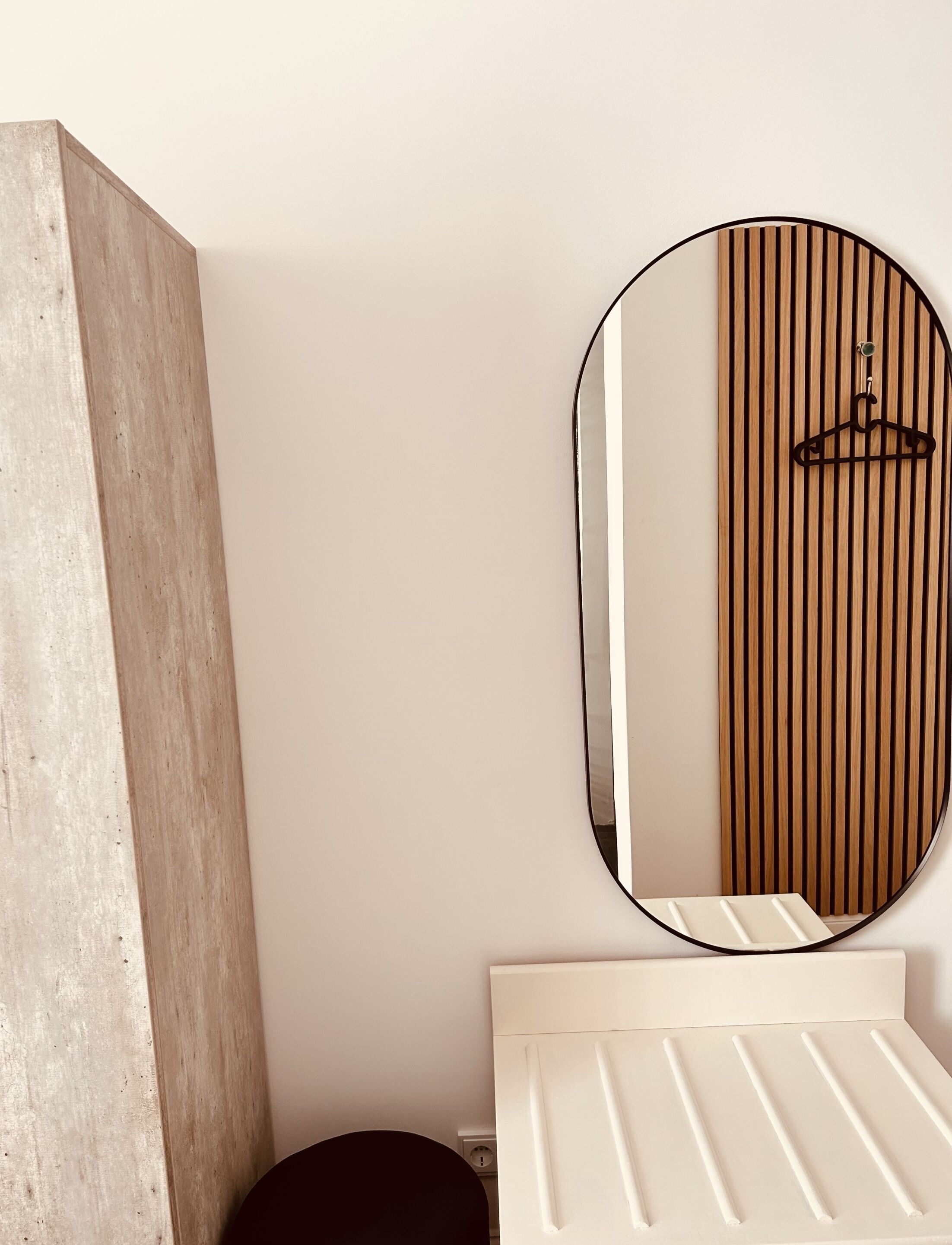 Ein Badezimmer mit Holzhakenschrank, rundem Spiegel und weißem Waschbecken.