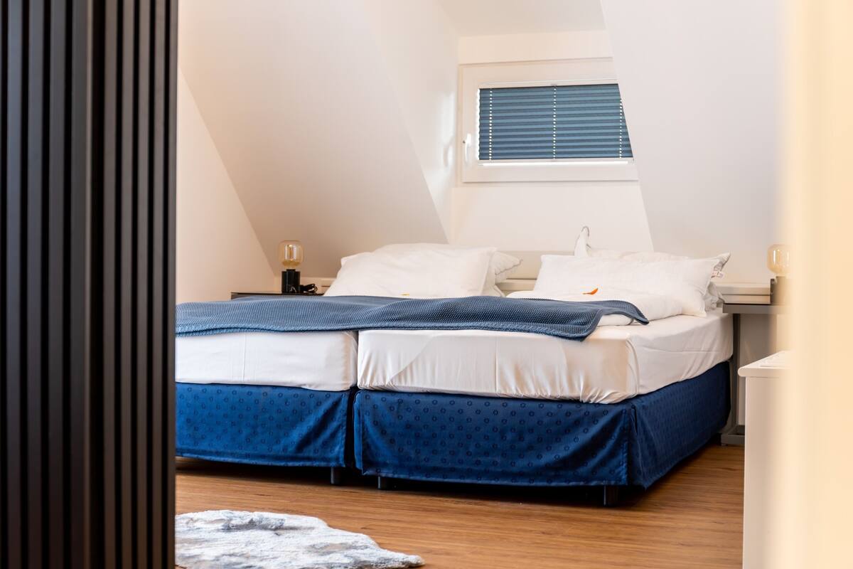 A bedroom with a bed, bedside tables, a window, and a view of the outside.