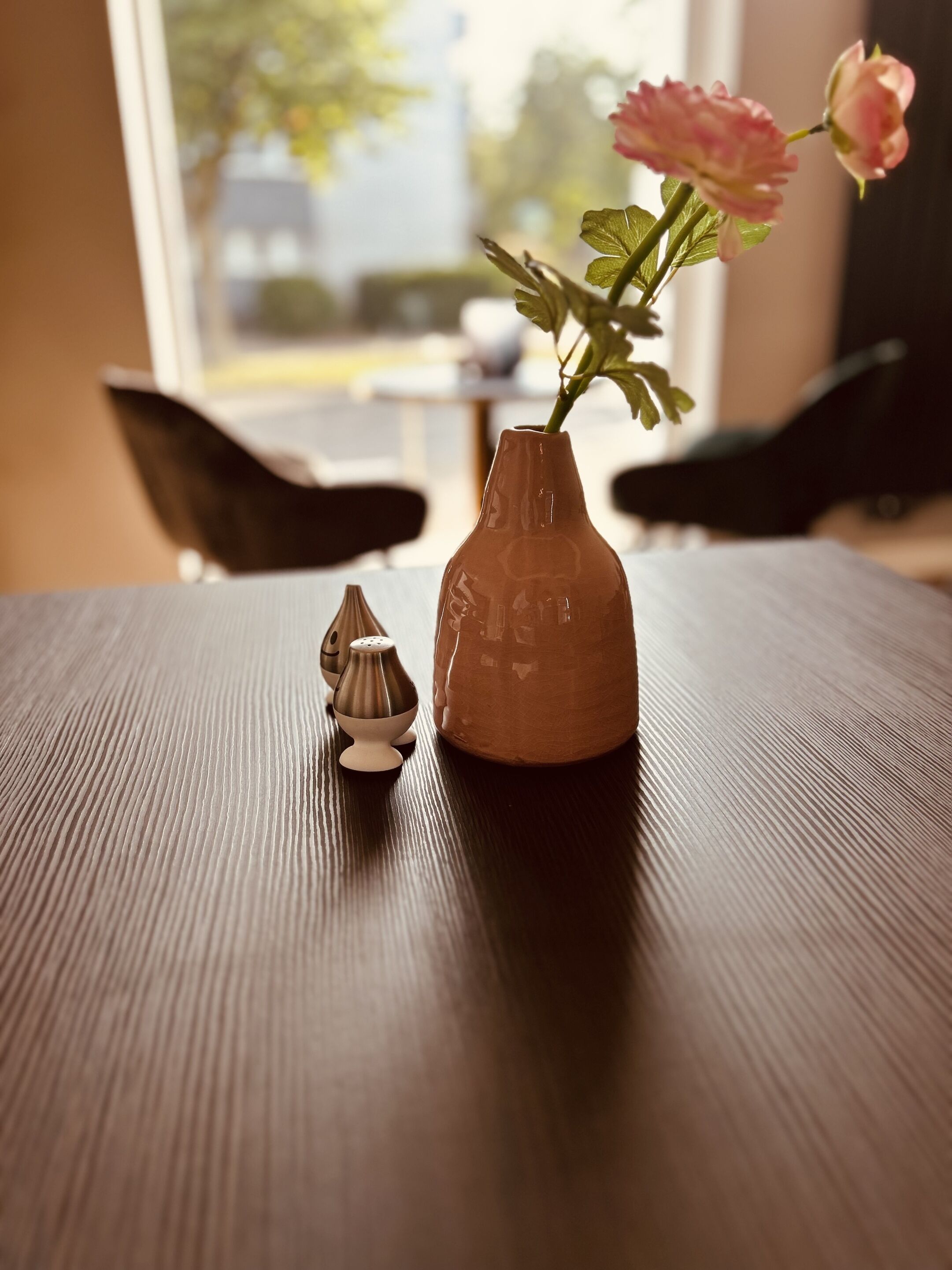 A wooden table with a ceramic vase and a salt shaker.