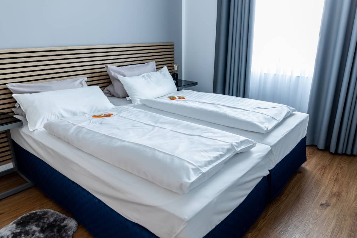 A double bed with white linens, a wooden headboard, and a nightstand with a lamp.