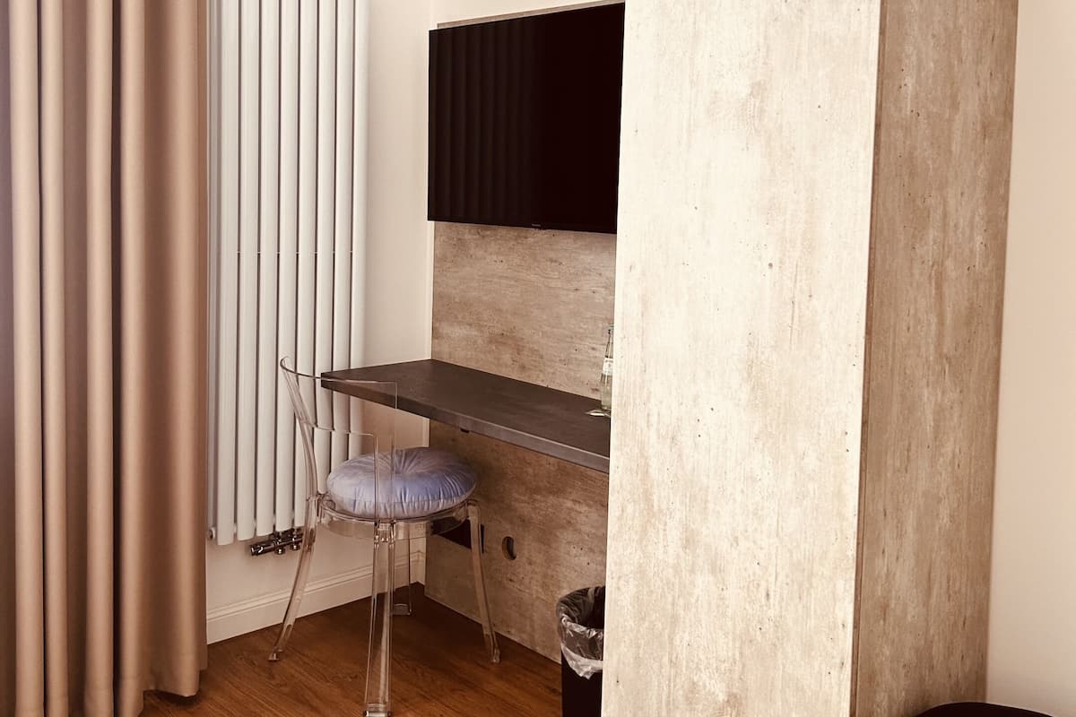 A small, modern room with a wooden desk, a chair, a radiator, and a large window with curtains.