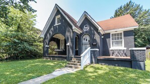 A two-story house with a dark exterior, a front porch, and a small front yard. - Midtown Tiger Retreat with ShellCrestCorp" 745 (Memphis)