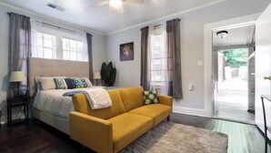A bedroom with a bed, a yellow sofa, a ceiling fan, and a door leading to a balcony. - Midtown Tiger Retreat with ShellCrestCorp" 745 (Memphis)