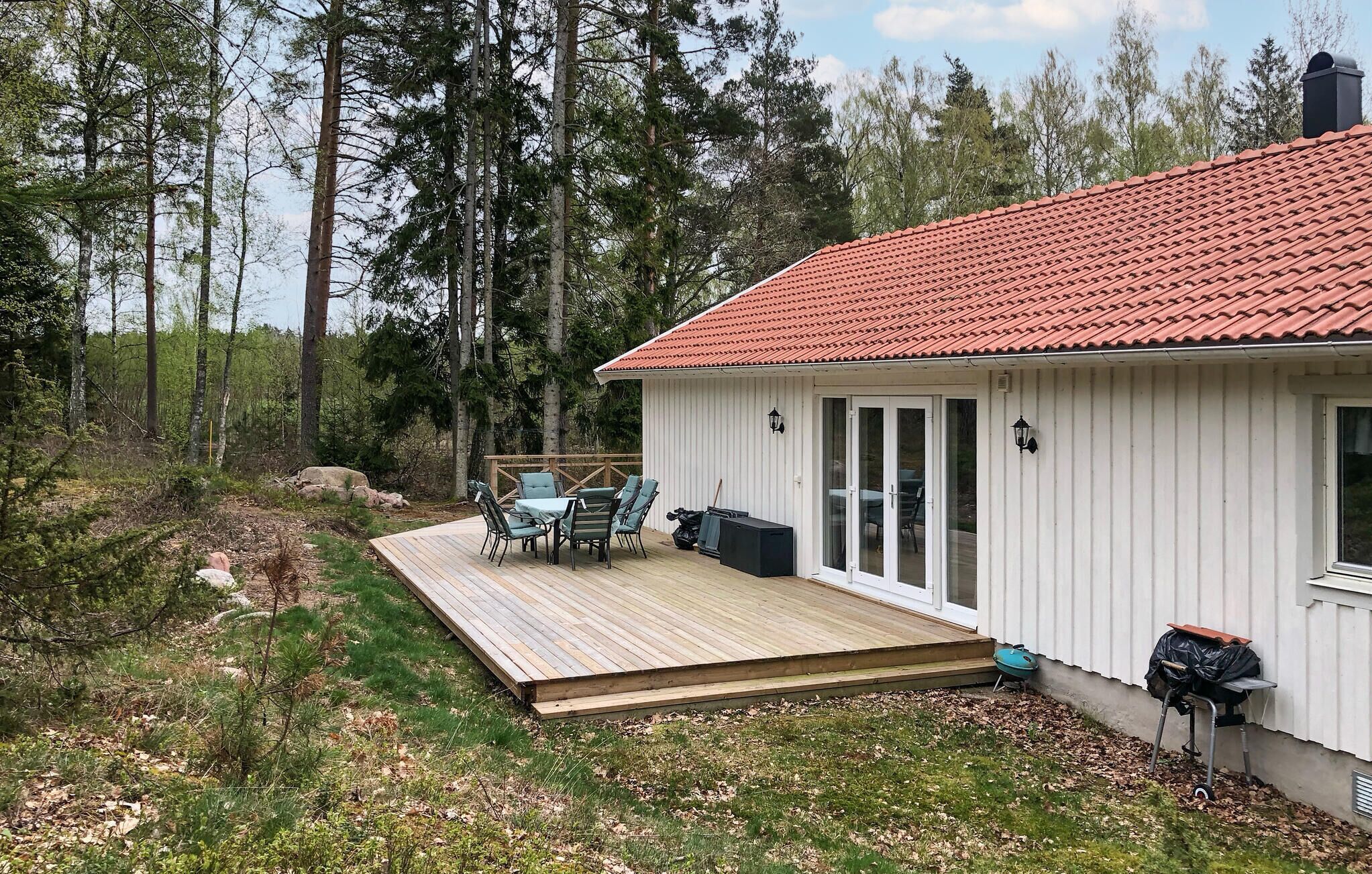 A cabin with a red-tiled roof, a deck with outdoor furniture, and a surrounding forest.