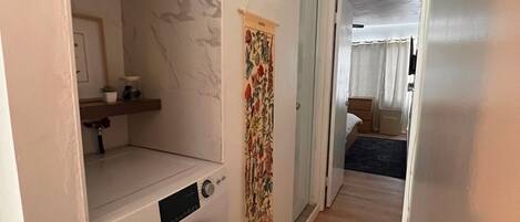 A laundry room with a washing machine, a drying rack, and a mirror.