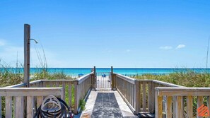 A wooden boardwalk leading to a beach with clear blue water and a grassy area.