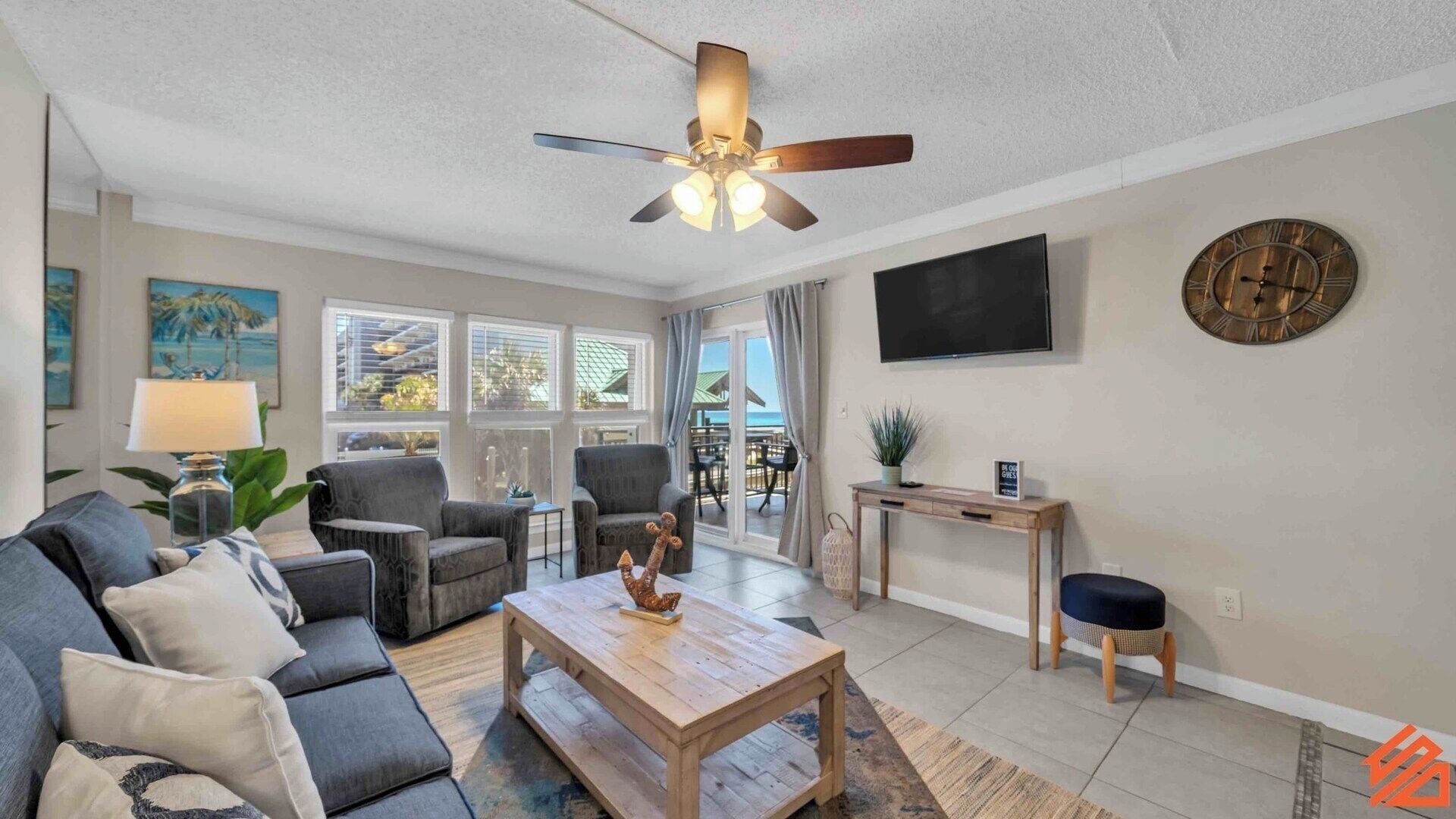 A living room with a sofa, chairs, a coffee table, a ceiling fan, a TV, and a clock on the wall.