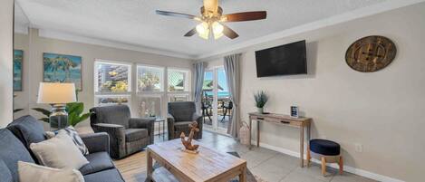 A living room with a sofa, chairs, a coffee table, a ceiling fan, a TV, and a clock on the wall.