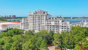 A multi-story hotel with a central courtyard, surrounded by lush greenery and a view of the water. - The Grand in SanDestin Resort Luxury 1BR Condo (Miramar Beach)