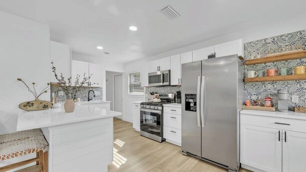 Una cocina moderna con armarios blancos, un refrigerador de acero inoxidable, un microondas y un horno.