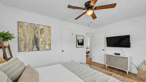 Un dormitorio con una cama grande, un ventilador de techo, un televisor y un cuadro en la pared.