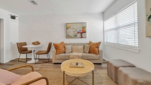 Een moderne woonkamer met een bank, salontafel en stoelen. Er hangt een schilderij aan de muur en een raam met zonwering.