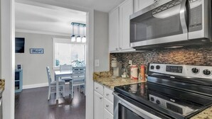Een moderne keuken met roestvrijstalen apparatuur, granieten aanrecht en een eethoek met witte stoelen.