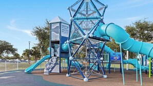 Une aire de jeux avec une structure d’escalade, des toboggans et une cabane à jouer portant l’inscription « DESTIN FORT WALTON BEACH FLORIDA ».