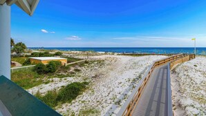 Une vue sur la plage, avec une promenade en bois, des dunes de sable et un ciel bleu dégagé.