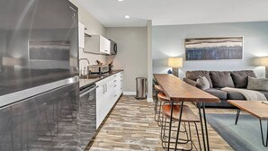Une cuisine moderne avec un réfrigérateur en acier inoxydable, des armoires blanches et une table à manger en bois, accompagnée de tabourets de bar.