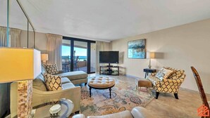 Habitación de hotel moderna con sofá, reposapiés y sillón, televisor de pantalla plana y vista al océano.