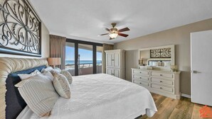 Un dormitorio con cama, ventilador de techo, cómoda y vista al océano.