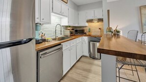 A compact kitchen with white cabinetry, a stainless steel refrigerator, a microwave, and a dishwasher. - Okaloosa Island White Sand Beach 1BR Condo Getaway (Fort Walton Beach)