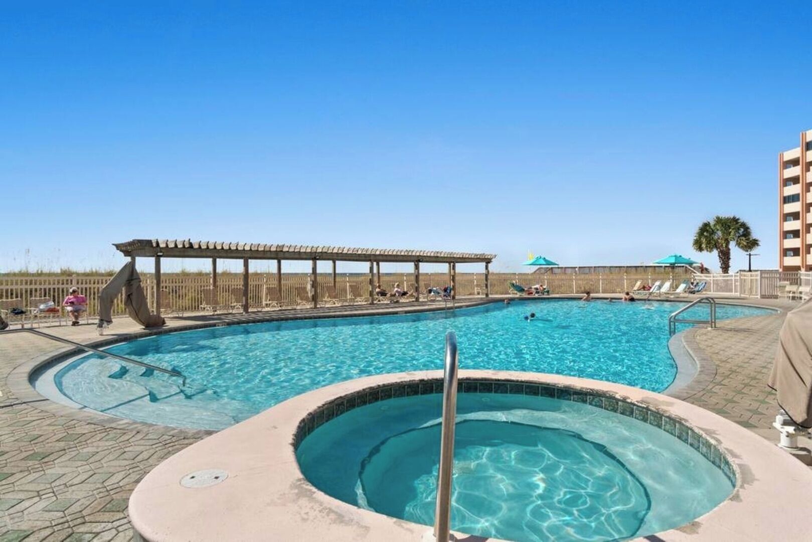 A large outdoor swimming pool with a hot tub, lounge chairs, and a covered area.