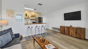 Ein modernes Wohnzimmer mit Sofa, Couchtisch und einer Küchenzeile mit Barhocker.