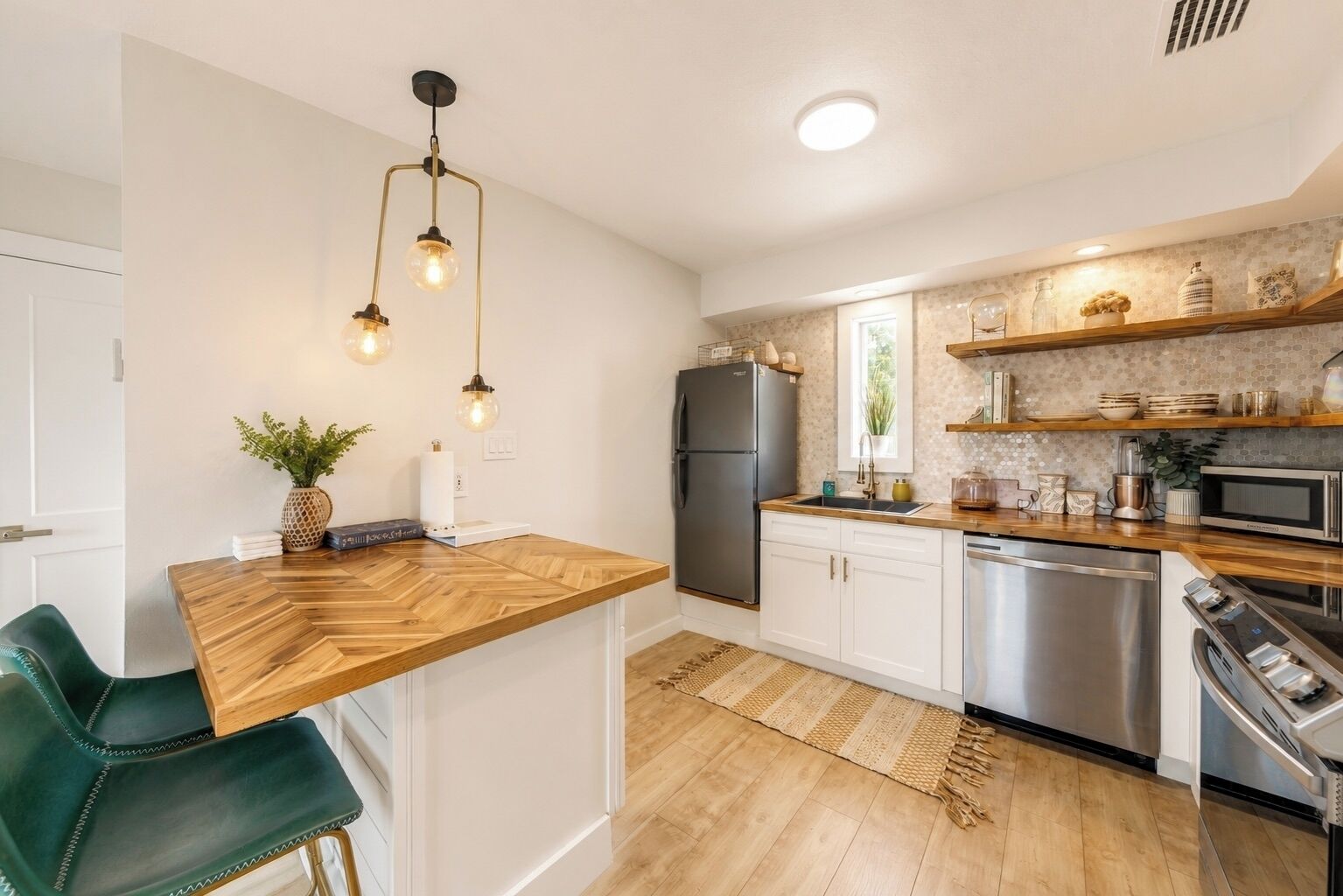 Una cucina moderna con un piano di lavoro in legno, elettrodomestici in acciaio inossidabile e illuminazione a sospensione.