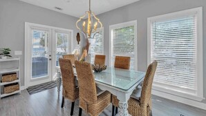 A dining area with a glass table, wicker chairs, and a chandelier. - Large 3BR Family Destin Beach House w Beach Access (Destin)