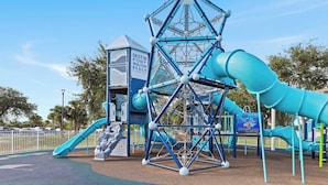 Un parque infantil con una estructura para escalar, toboganes y una casita, identificada como 'DESTIN FORT WALTON BEACH FLORIDA'.