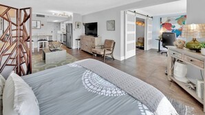 Una habitación de hotel moderna con una cama grande, un escritorio, una silla, un televisor y una zona de cocina.
