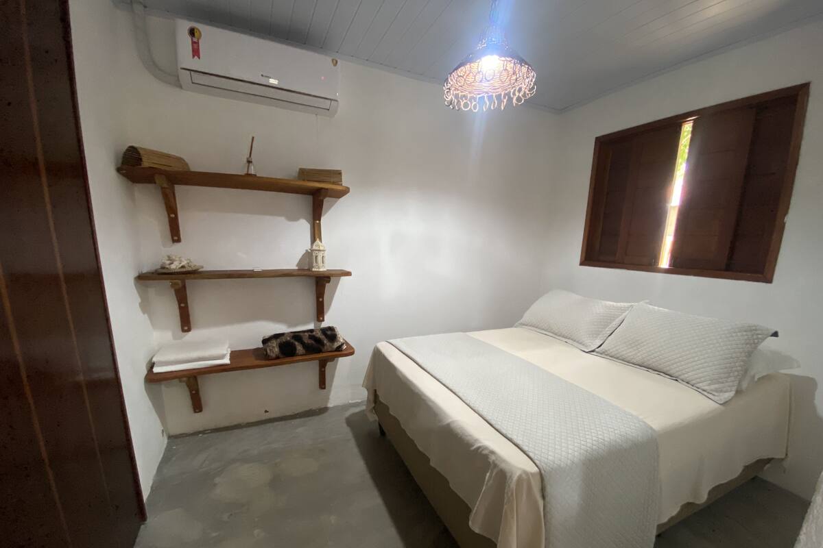 Ein Schlafzimmer mit einem Bett, Holzregalen, einer Pendelleuchte und einem Fenster mit Jalousien.