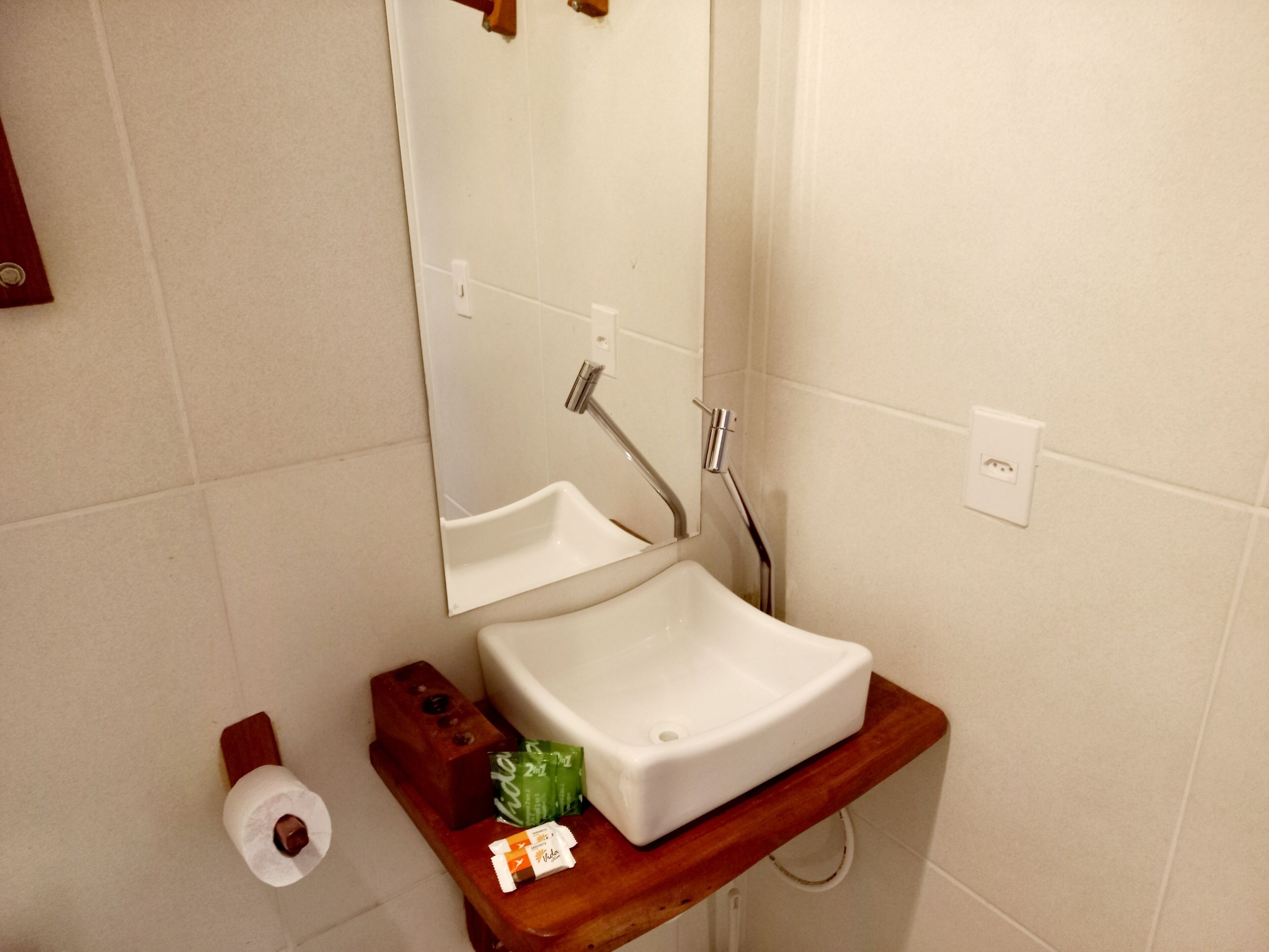 A bathroom with a white sink, a mirror, and a wooden shelf with toiletries.