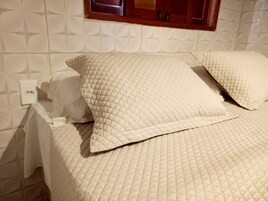 A bed with a quilted white bedspread and pillows, a wooden headboard, and a wall socket.