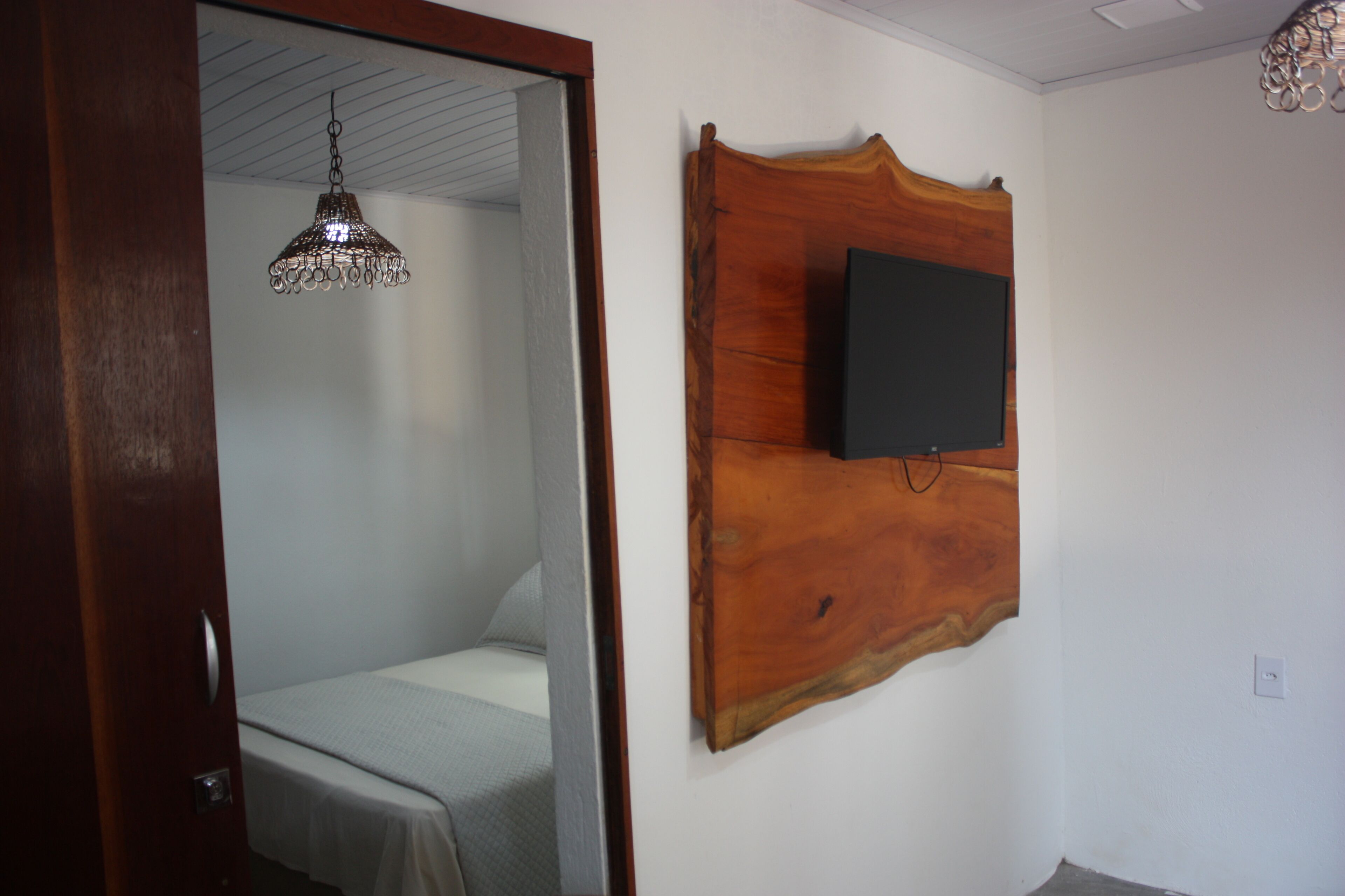 A bedroom with a bed, a wooden headboard, a television mounted on the wall, and a hanging light fixture.