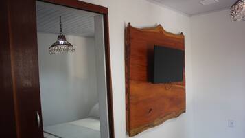 A bedroom with a bed, a wooden headboard, a television mounted on the wall, and a hanging light fixture.
