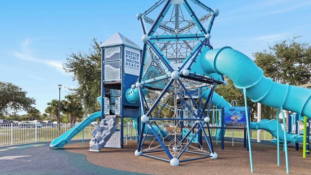 Un parque infantil con una estructura para escalar, toboganes y una casita, identificada como 'DESTIN FORT WALTON BEACH FLORIDA'.