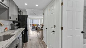 A modern kitchen with grey cabinets, a black refrigerator, and a marble countertop.