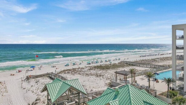 A beach view with a pool, beach umbrellas, and a lifeguard stand.