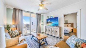 A hotel room with a balcony, a sofa, a coffee table, a TV, and a bed.