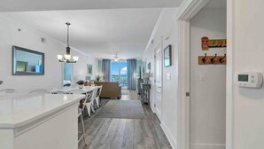 A modern kitchen with a dining area, a living room with a view, and a hallway leading to a bedroom.