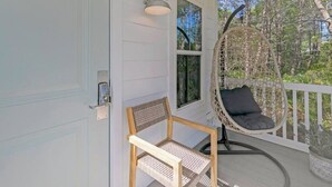 A porch with a wicker chair, a wooden table, and a hanging chair with a cushion.