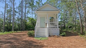 A small, single-story cabin with a porch, surrounded by a forested area.