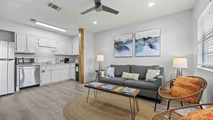 Una sala de estar moderna con un sofá gris, dos mesas auxiliares con lámparas, una mesa de centro y una silla de mimbre.