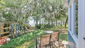 A patio with a table and chairs, surrounded by trees with hanging moss, a wooden fence, and a view of a body of water.