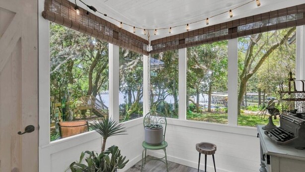 A sunroom with large windows, a wooden floor, and a typewriter on a desk.