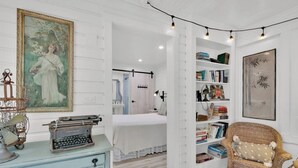 A room with a vintage typewriter, a wicker chair, a bookshelf, and a painting on the wall.
