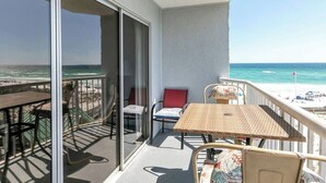 Un balcón con vistas a la playa, una mesa, sillas y un ventanal.