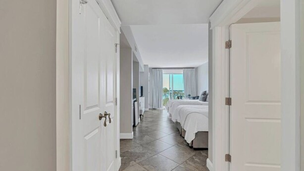 Un pasillo de hotel con puertas blancas, piso de baldosas y un balcón con vistas.