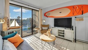 Ein modernes Wohnzimmer mit einem großen Fernseher, einer Couch, einem Couchtisch und Blick auf einen Pool durch eine Schiebetür.