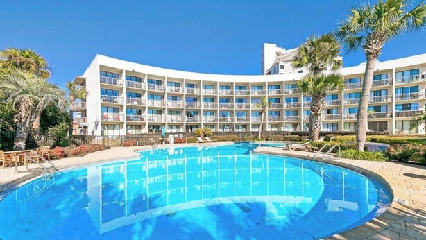 Ein Hotel mit großem Pool, Palmen und blauem Himmel.